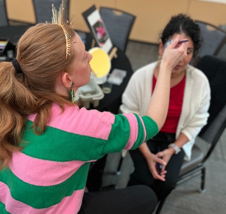 Mallory painting a flower on the side of an employee's face